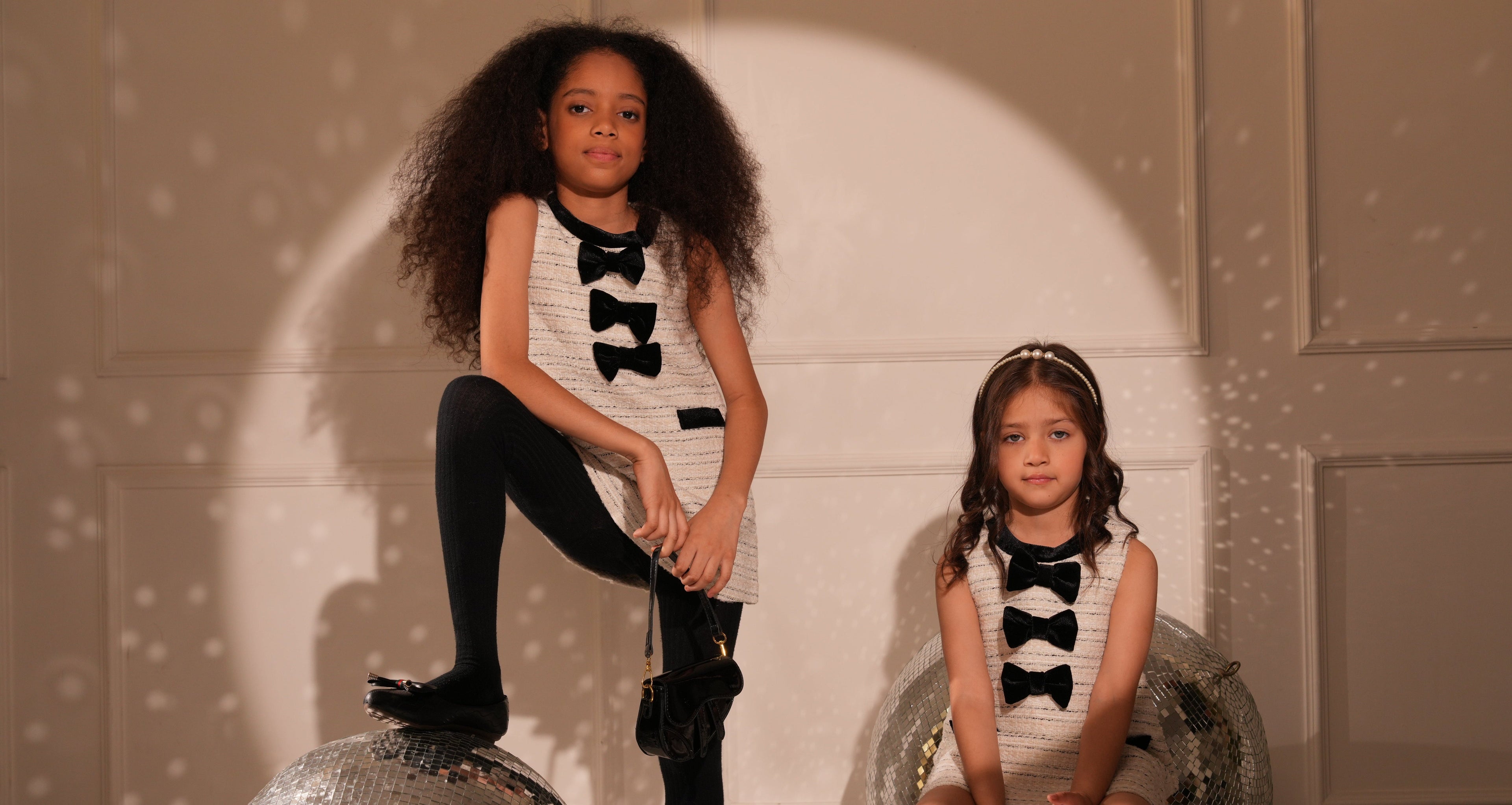 Two young girls in matching outfits sitting on a disco ball with a spotlight effect.