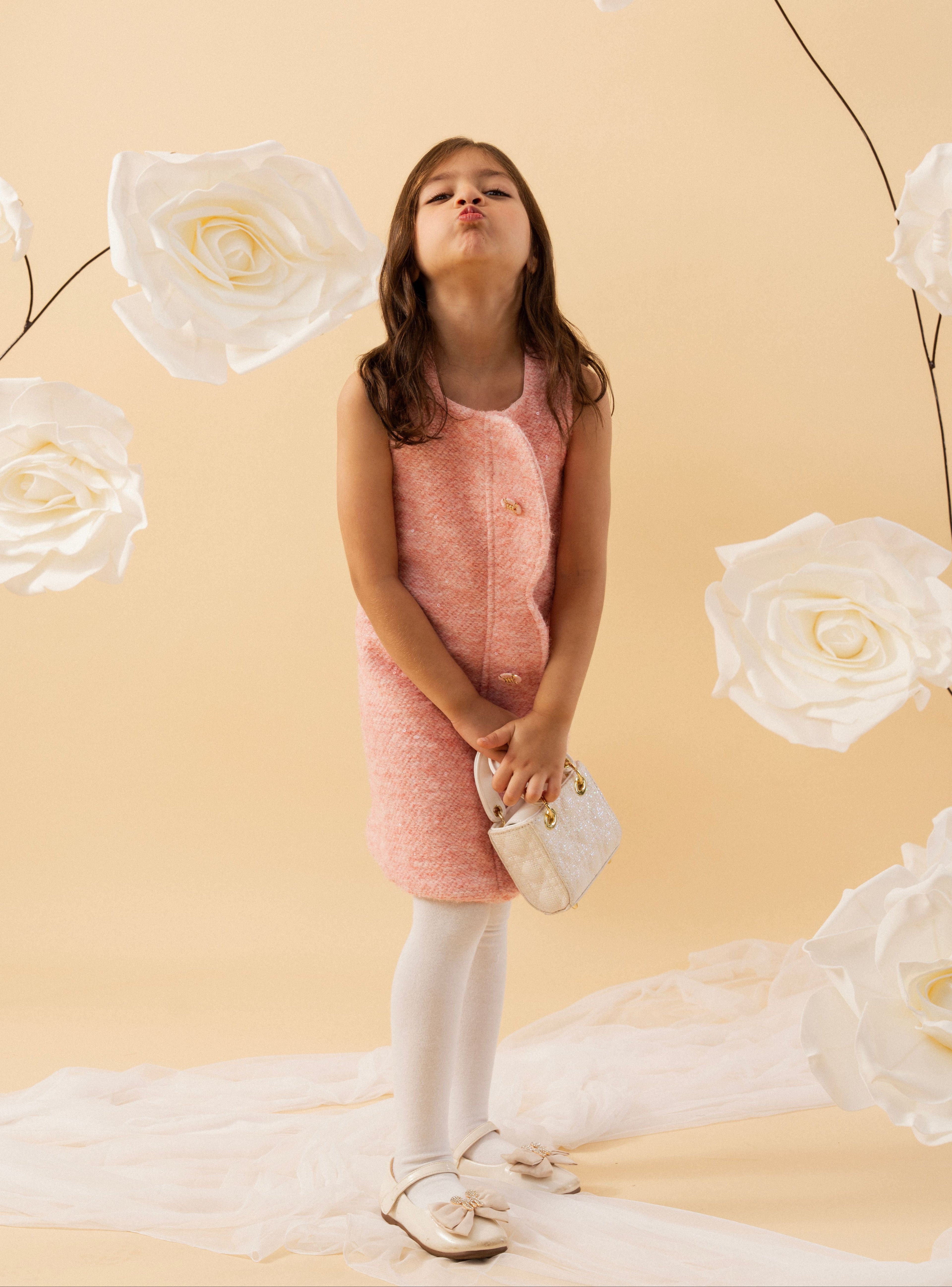 Young girl in a pink dress standing against a beige background with large white flowers.